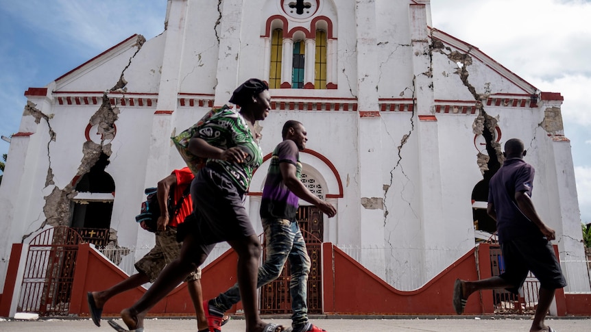 People run scared past a building that is severely cracked and damaged in Haiti 