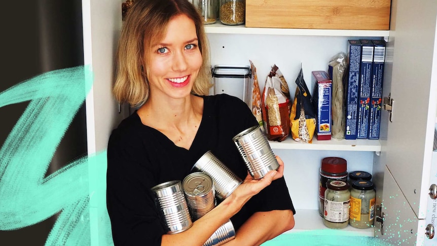 Young woman holding cans of food while standing in front of her pantry in a story about how to cook with canned food.
