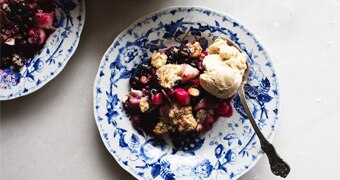 A serving of pear and blueberry crumble on a plate with a scoop of ice cream for a seasonal spring dessert.