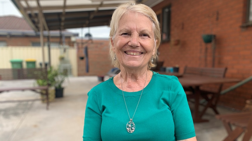 A smiling woman sits outside wearing a green top.