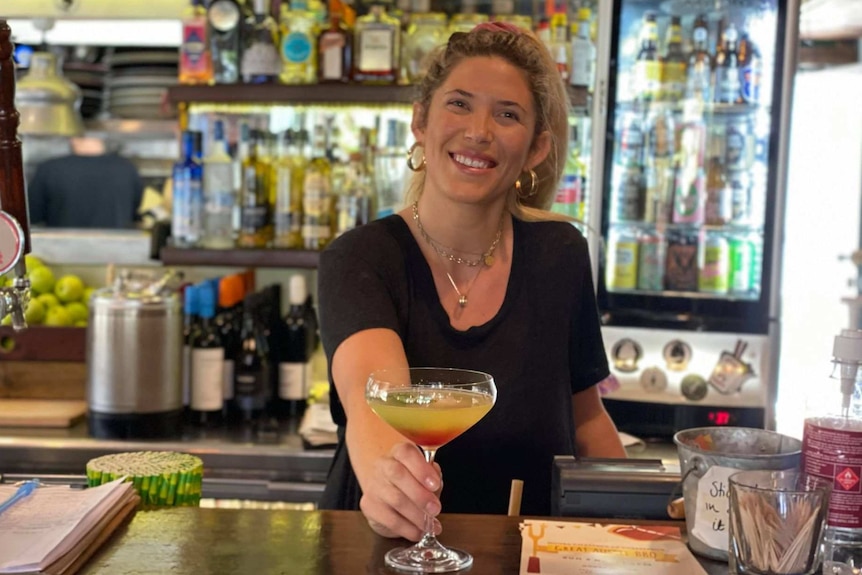 A woman serving a cocktail from behind a bar in Noosa