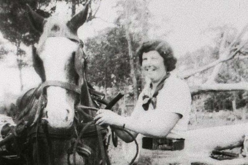 A woman in the 1940s with short hair and a white horse smiling beside a horse.