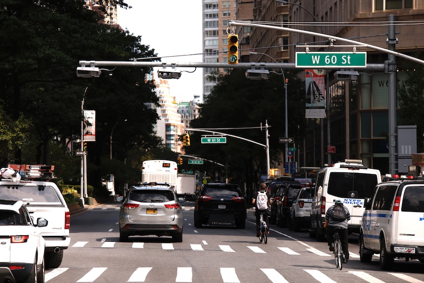 A photo of a New York midtown street during the day, with traffic lights, cars and cyclists