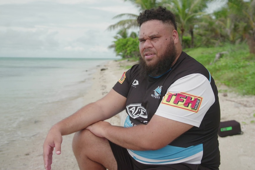 Man wearing jersey sitting on the shore of a beach.