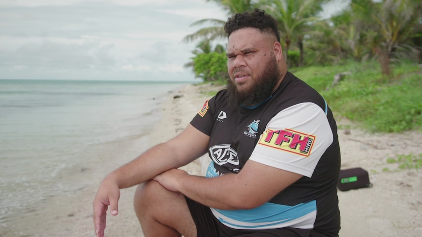 Man wearing jersey sitting on the shore of a beach.