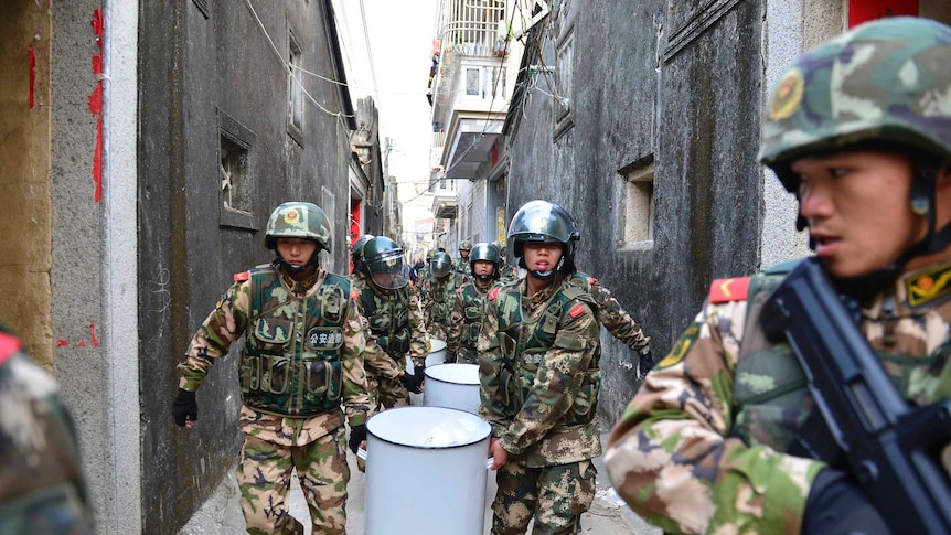 Policemen carry buckets of crystal meth down a narrow street during a raid.
