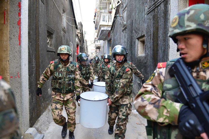 Policemen carry buckets of crystal meth down a narrow street during a raid.