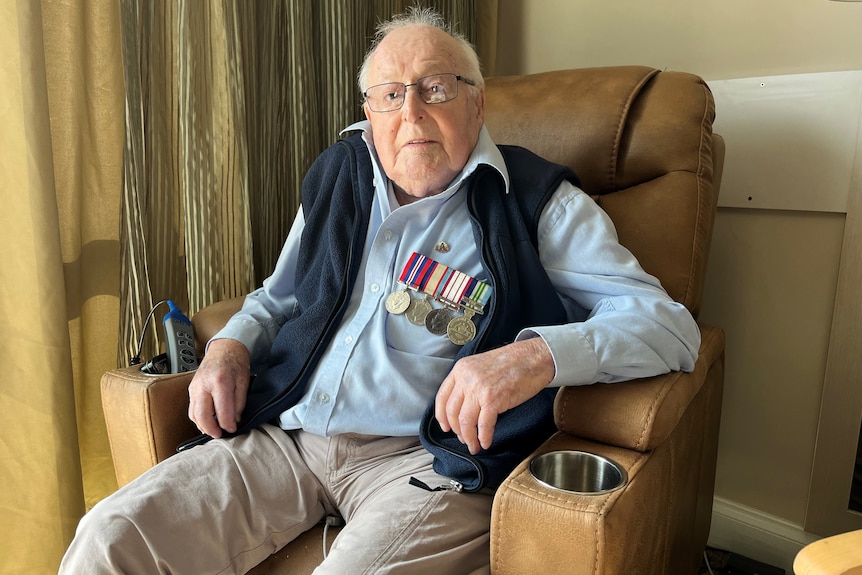 An elderly man sitting in a chair wearing four medals