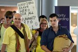 Ashley Dyball and his parents walk through Brisbane airport, while his mum holds a sign reading: "brave hero for all humanity".