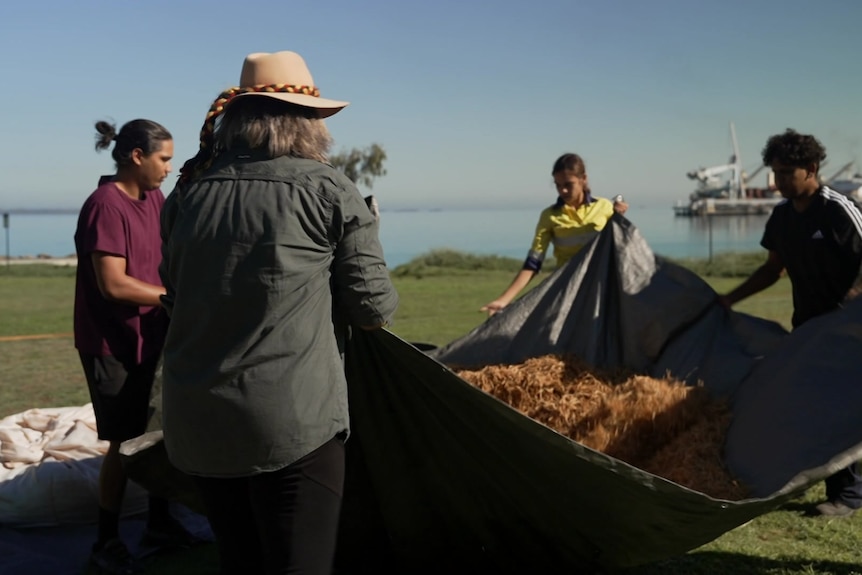 Photo of a group of people shaking wattle seeds in a tarp.