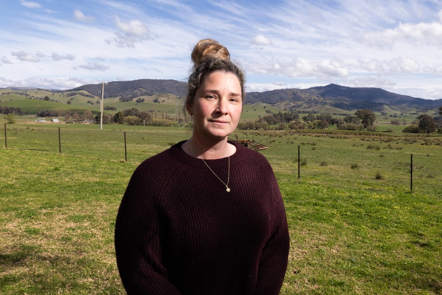 A woman stands in front of green paddocks 