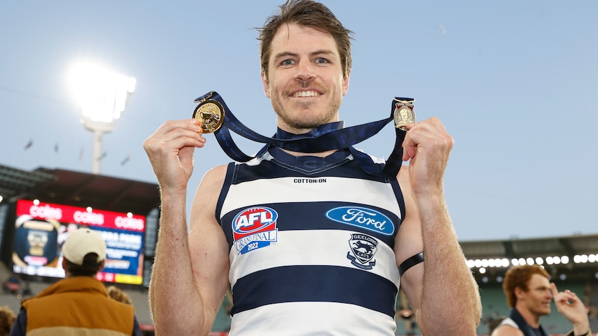 Isaac Smith smiles while holding up two medals which are hanging around his neck