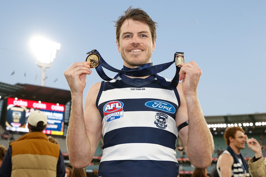 Isaac Smith smiles while holding up two medals which are hanging around his neck