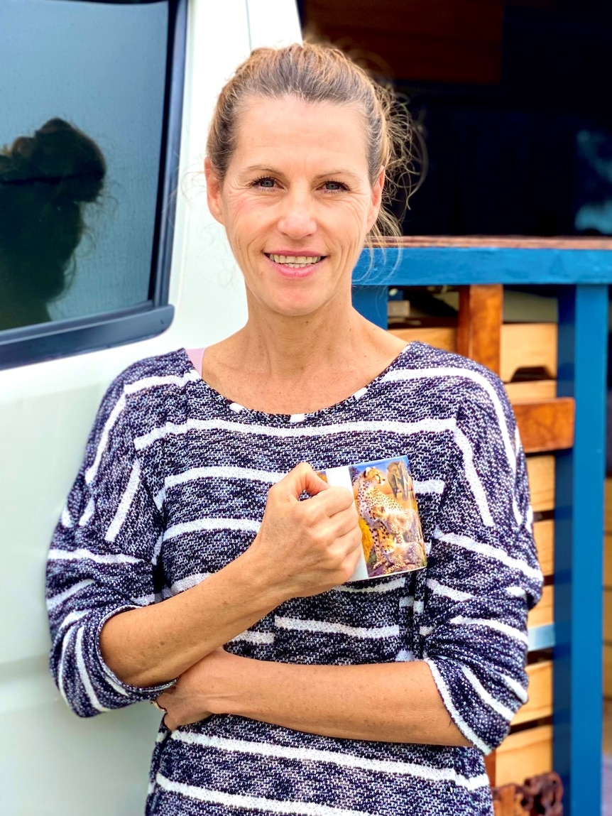 A woman in a striped top holds a mug while standing by a van door
