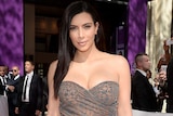 Full length photo of Kim Kardashian wearing a grey, figure-hugging dress, on the red carpet.