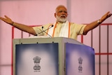 Narendra Modi gestures with arms wide and palms up as he speaks into two mics at a lectern.