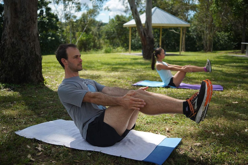 Personal trainer John McNaughton works with client Jasmin Lee about two metres from each other on floor mats.