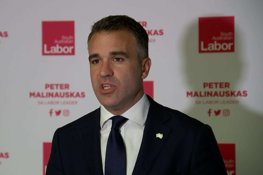 A man in a black suit and tie, in front of a banner reading "South Australian Labor" and "Peter Malinauskas".
