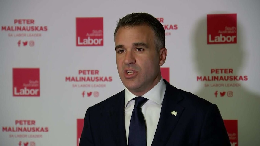 A man in a black suit and tie, in front of a banner reading "South Australian Labor" and "Peter Malinauskas".