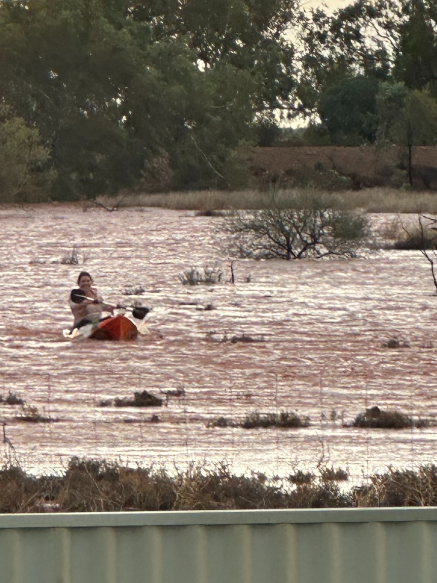 A woman kayaks through floodwater in a paddock.