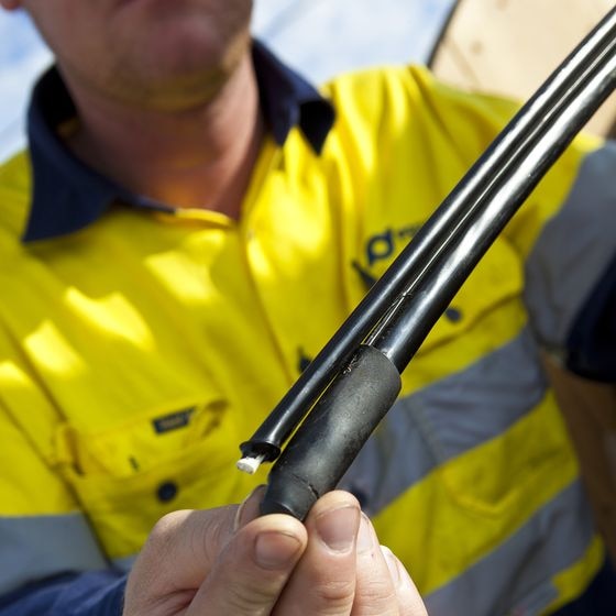 Hands hold an optic fibre wire during installation of Tasmania's NBN
