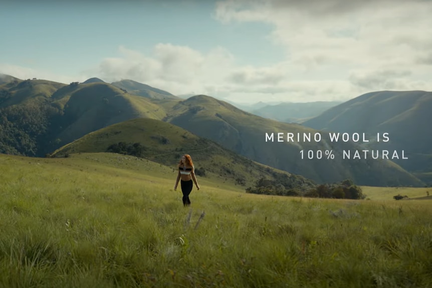 A woman walks through green fields wearing wool. 