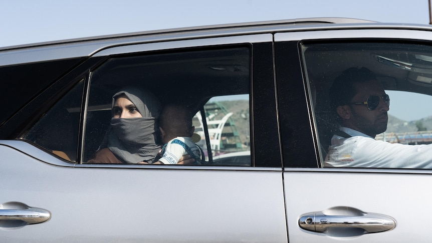 A woman in a headscarf holds a baby while looking out the window of a car 