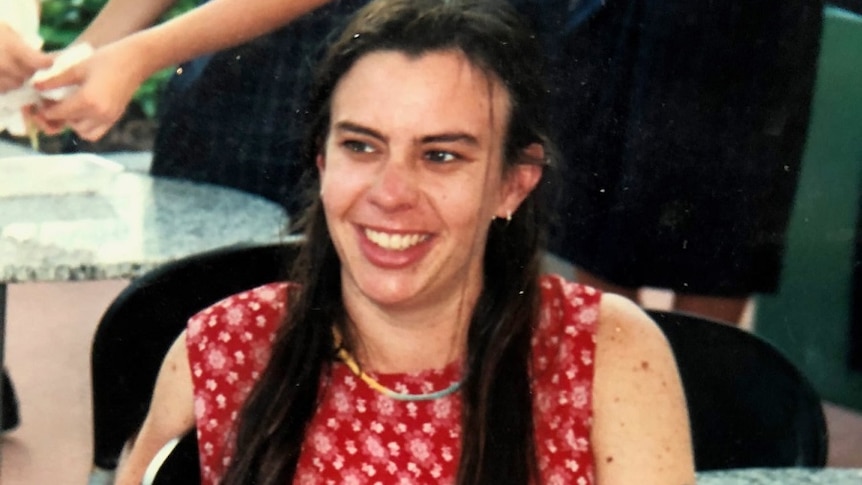 A woman with long brown hair sitting down, wearing a red dress with an arm tattoo