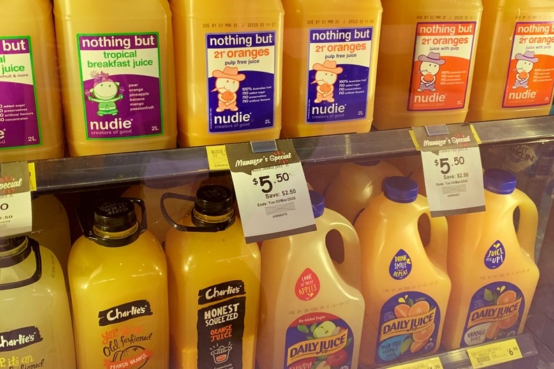 Large bottles of various brands of orange juice in a supermarket fridge