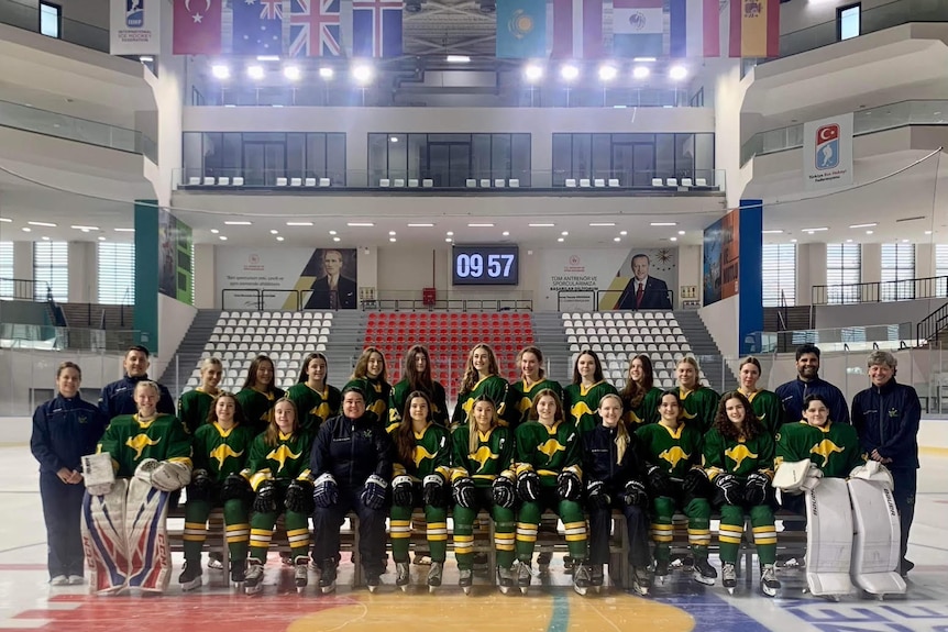 A team photo of the Australian under 18 girls ice hockey team sitting in two rows on the ice rink