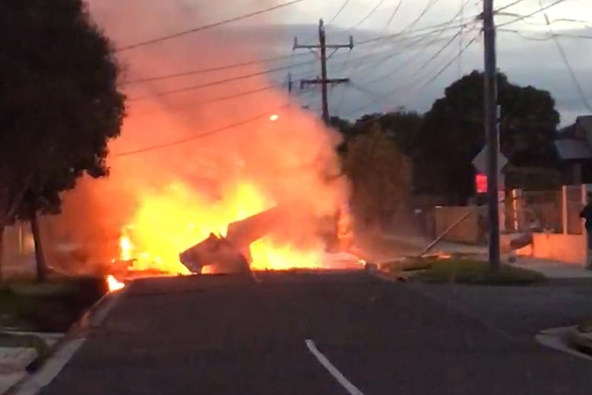 A screenshot showing a light plane on fire after crashing onto a street in Mordialloc.