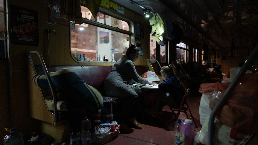 A mother and daughter sit together at a table on a stationary train