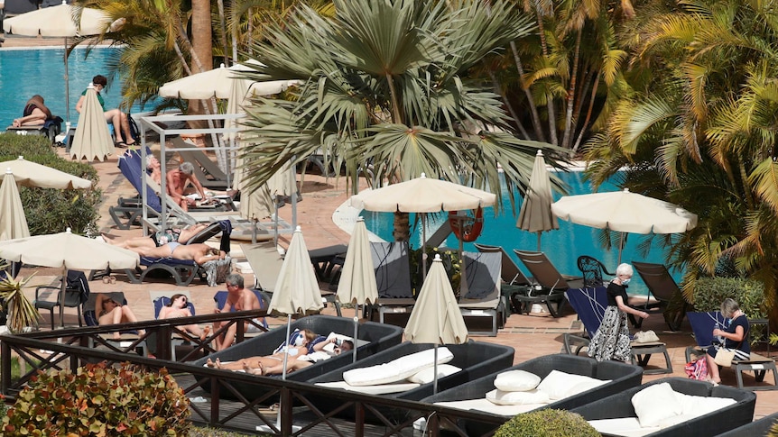 A photo taken from far away showing guests sunbaking by a hotel pool.