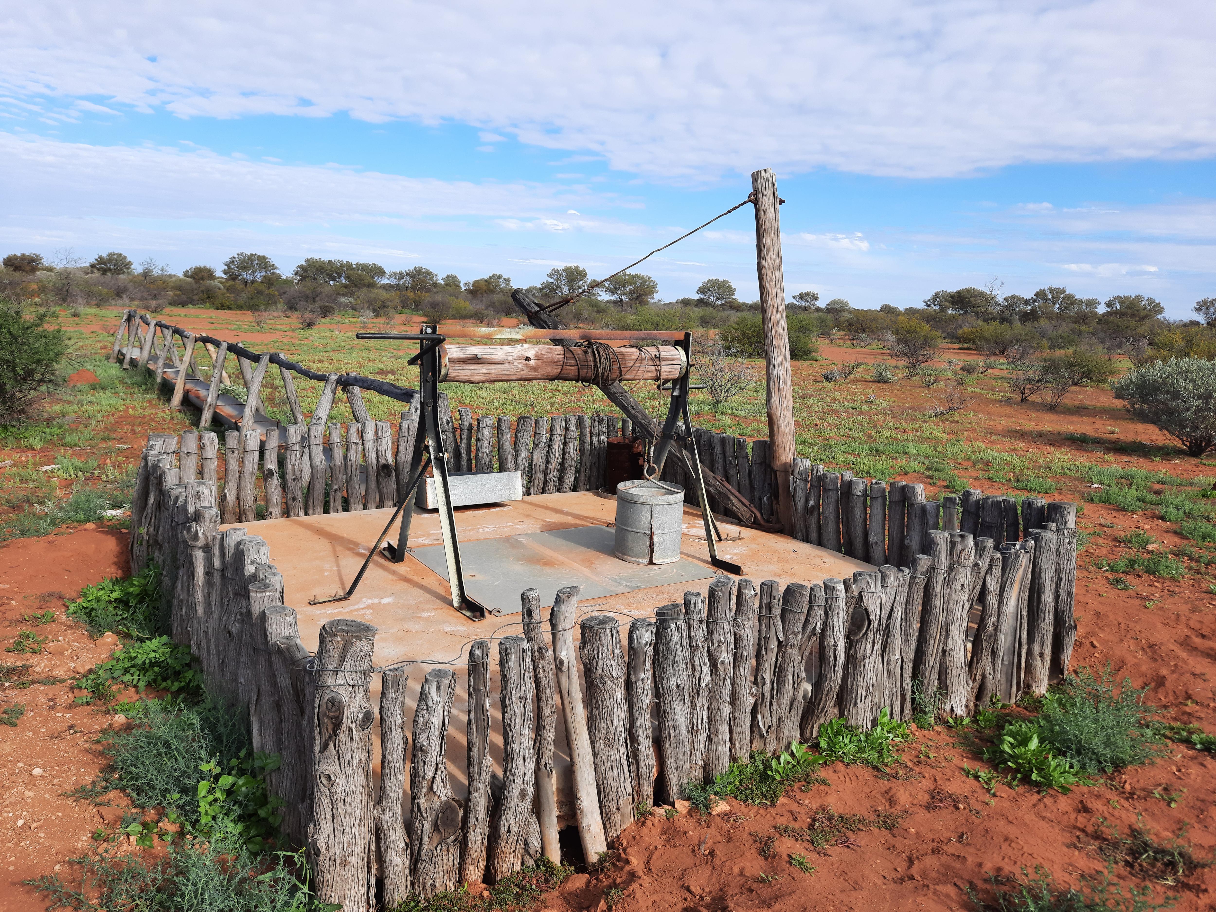 A well with a wooden fence around it in a red dirt landscape. 