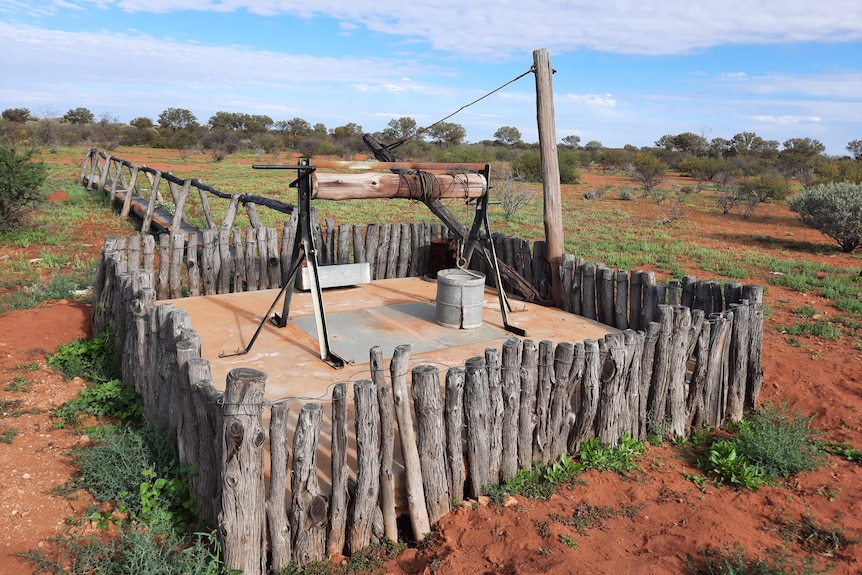 A well with a wooden fence around it in a red dirt landscape. 