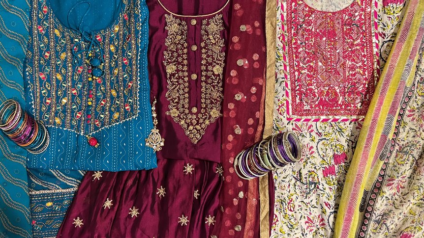 Three different three-piece outfits of various colours laid out flat with two sets of bangles placed on them