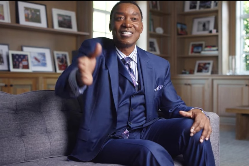 Detroit Pistons legend Isiah Thomas mimes shaking hands while sitting on a couch during an interview.