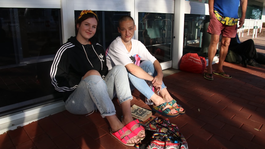 Two women sit on the floor outside a glass door