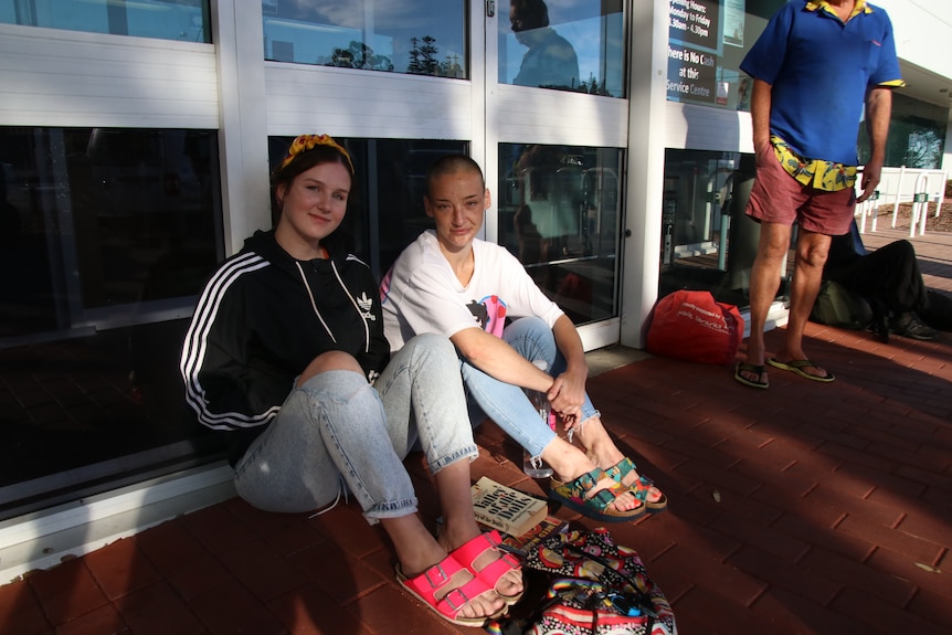 Two women sit on the floor outside a glass door