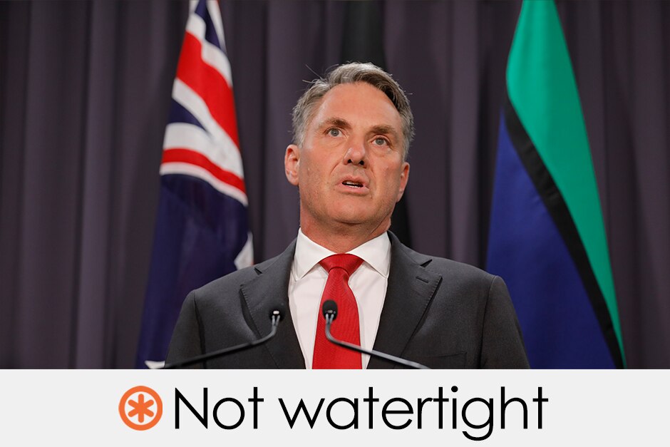 Richard Marles wears a suit and tie and speaks in front of Australian and Torres Strait Islander flags. VERDICT: Not watertight