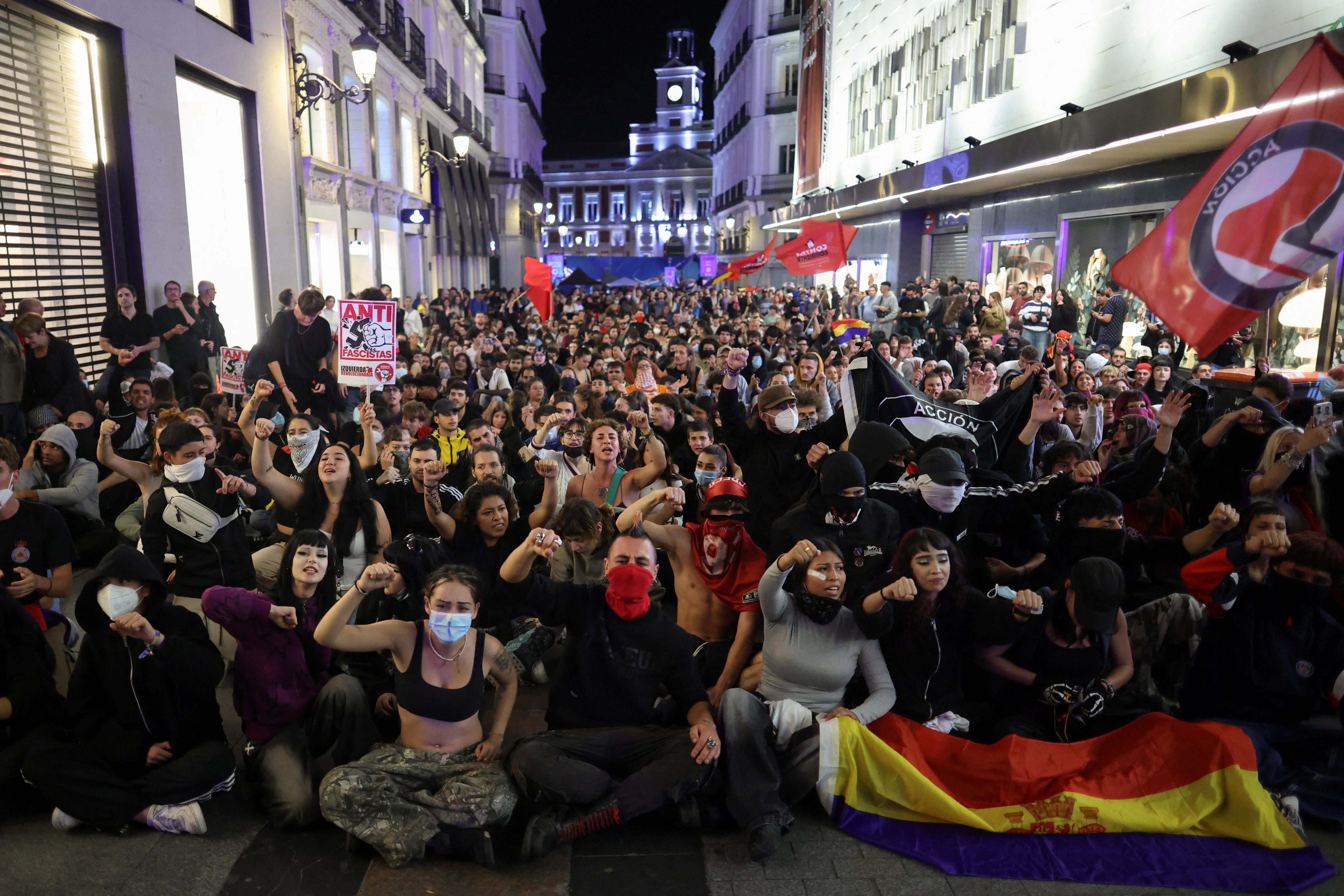 Hundreds of people are sitting down on a street leading to Puerta del Sol.