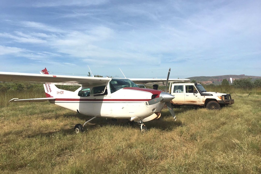 A light plane parked next to a ute in a far country