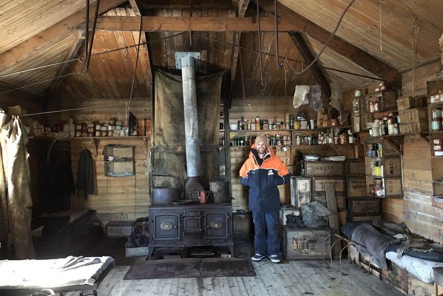 a man in snow gear standing inside an old wooden hut