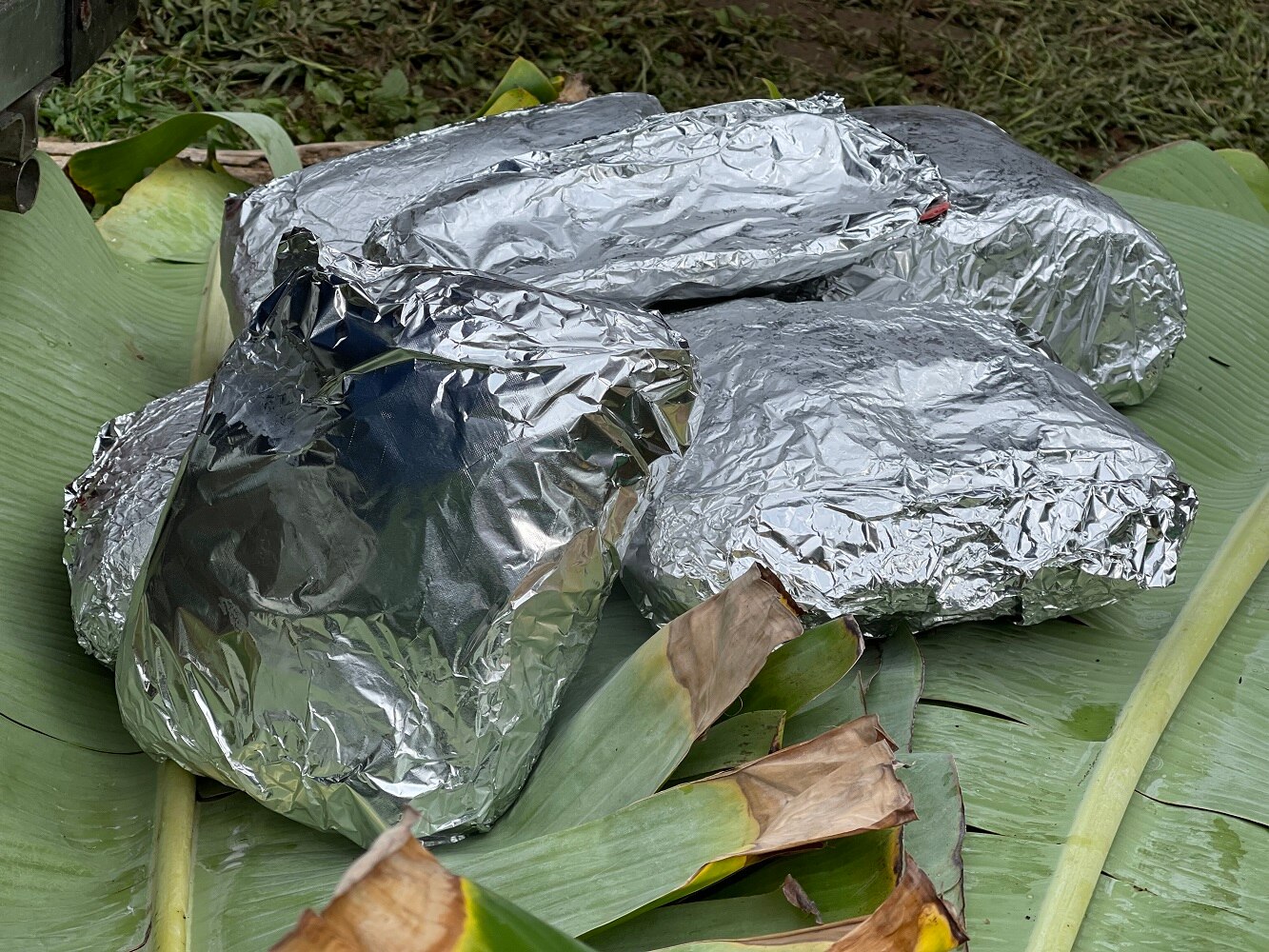 Meat wrapped in foil and resting on banana leaf.