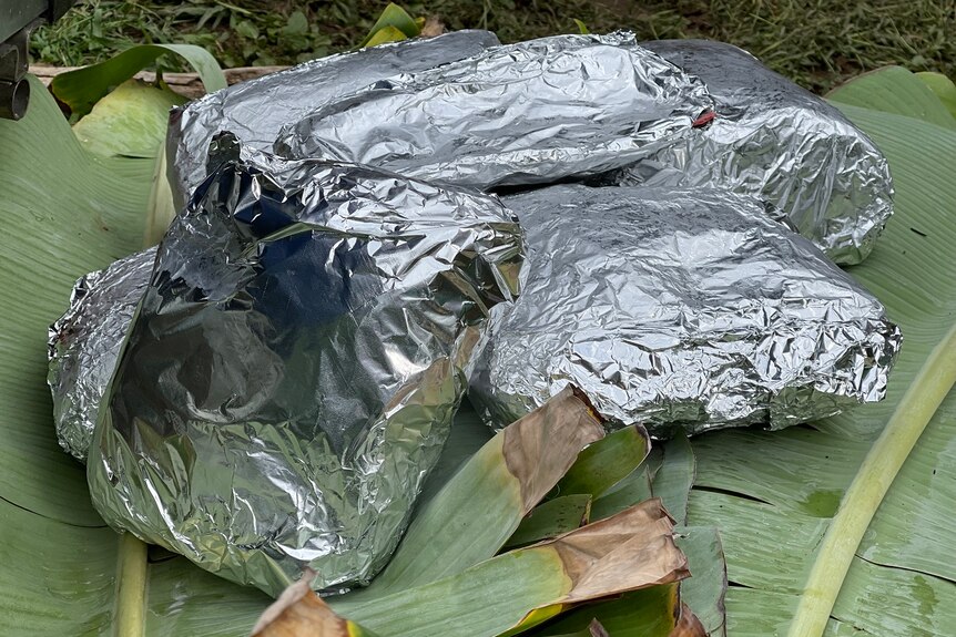 Meat wrapped in foil and resting on banana leaf.