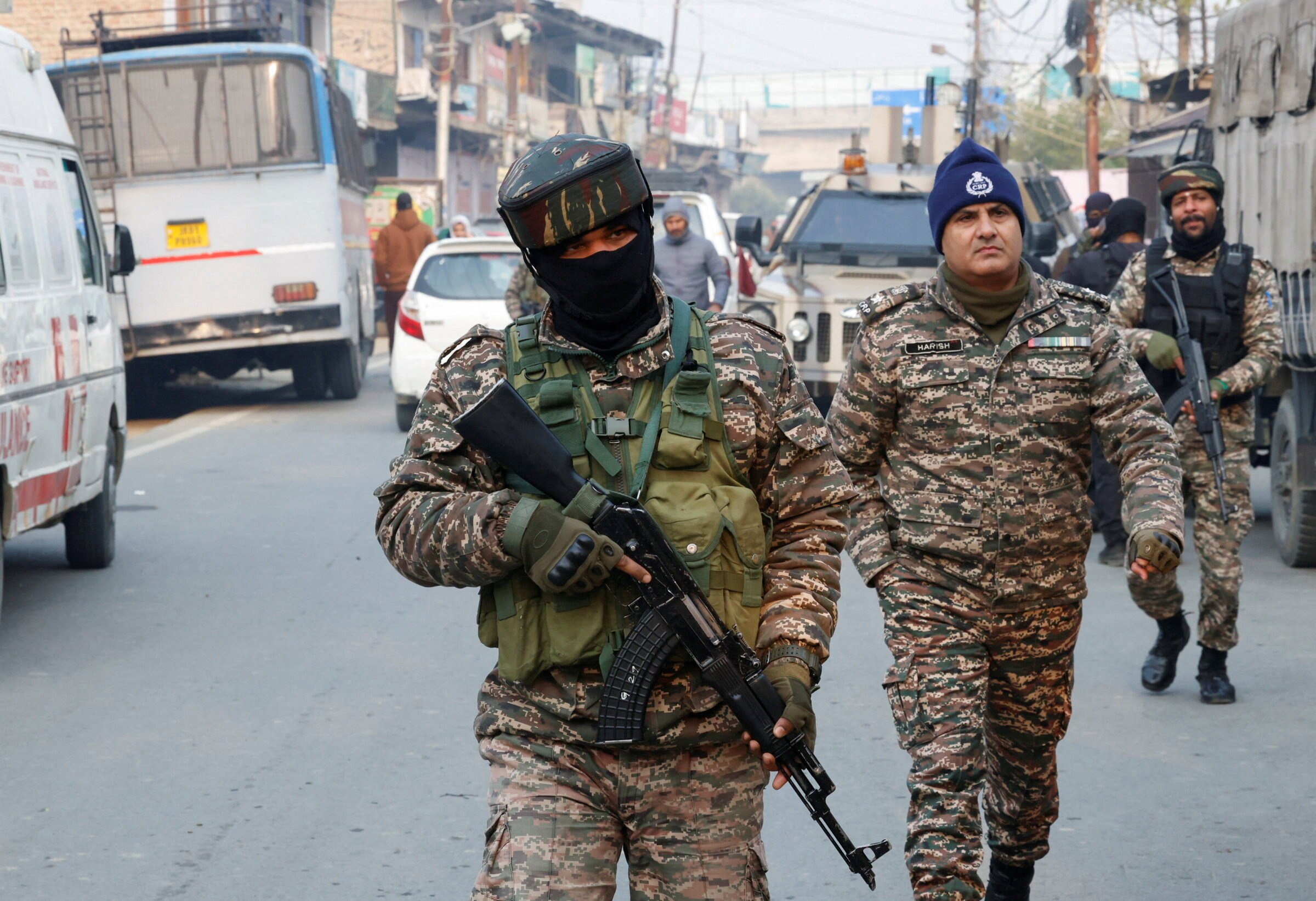 Três agentes de segurança caminham por uma rua, dois deles armados.