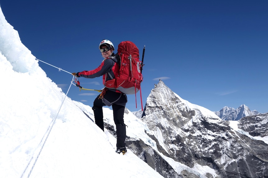 A woman holds ropes and carries a pack on a snowy mountain