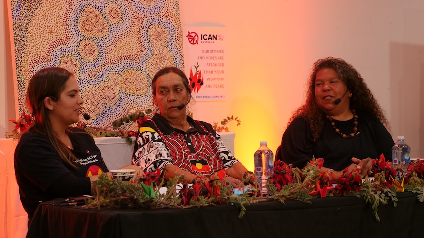 three women sititng at a table surrounded by flowers.