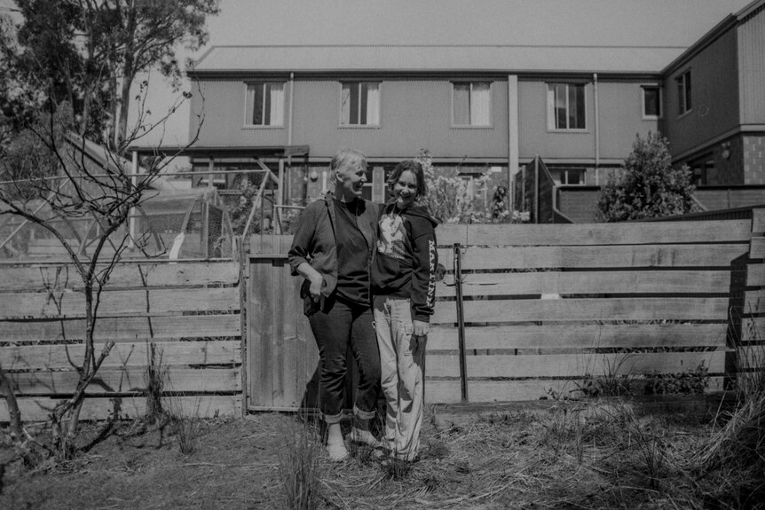 Mother and daughter hug and smile for camera in front of house 