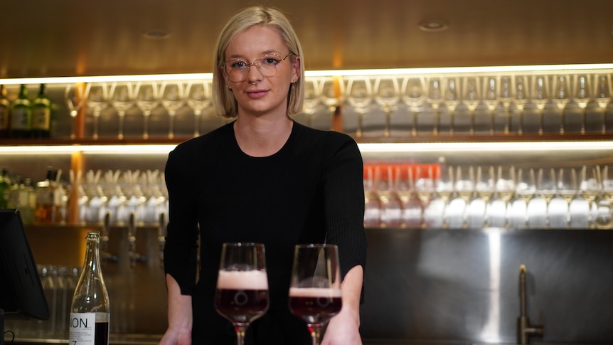 A woman standing behind a bar with wine glasses